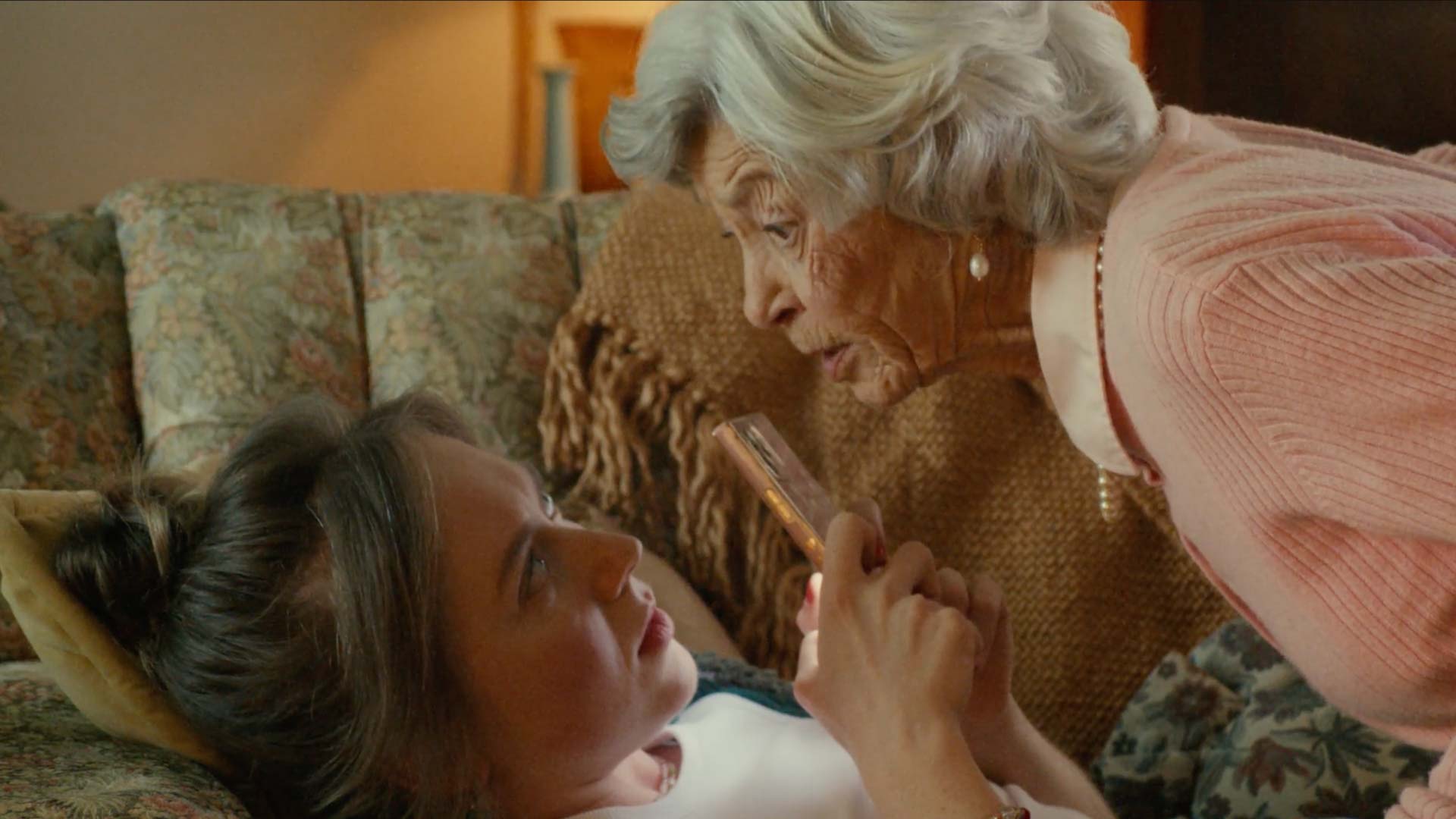 Still frame from "Granny" tv spot of white-haired well-kept granny leaning in hovering inches over her granddaughter who is lying on a sofa looking at her phone, but momentarily surprised by her granny.